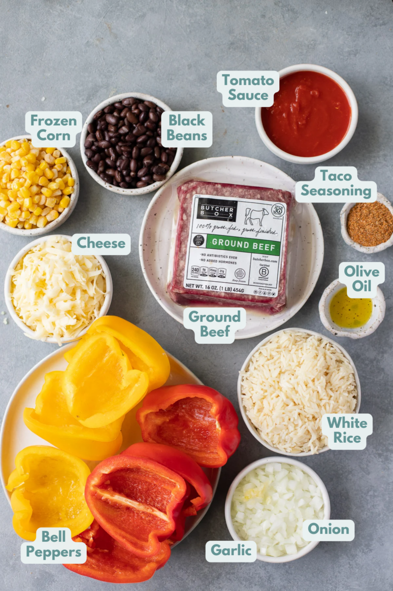 Ingredients for taco stuffed peppers in white bowls: olive oil, onion, garlic, butcher box ground beef (or ground turkey), bell peppers, tomato sauce, taco seasoning,  black beans, frozen corn, rice, cheddar cheese