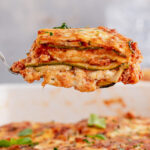 A piece of zucchini lasagna being lifted out of a casserole dish