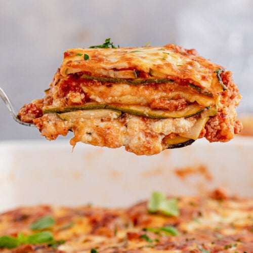 A piece of zucchini lasagna being lifted out of a casserole dish