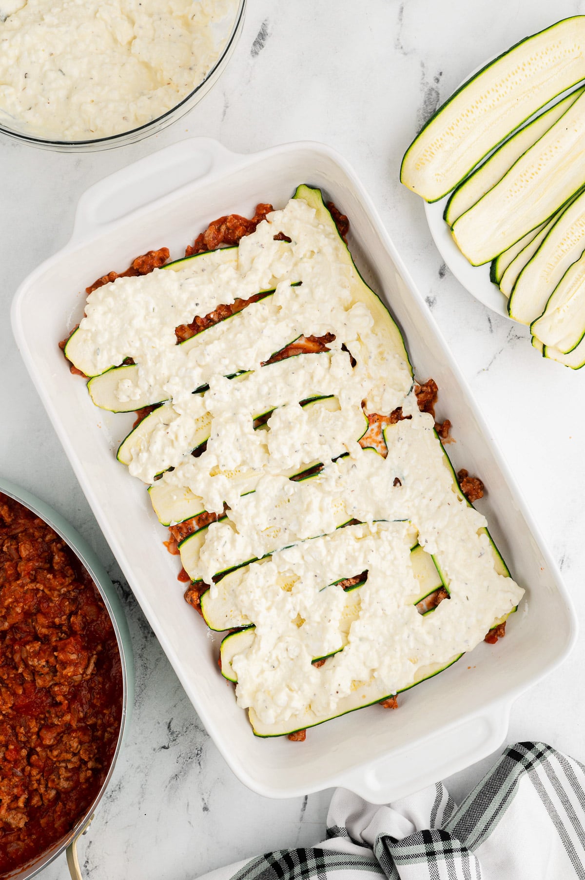 beginning layers of zucchini lasagna being layered in a white casserole dish