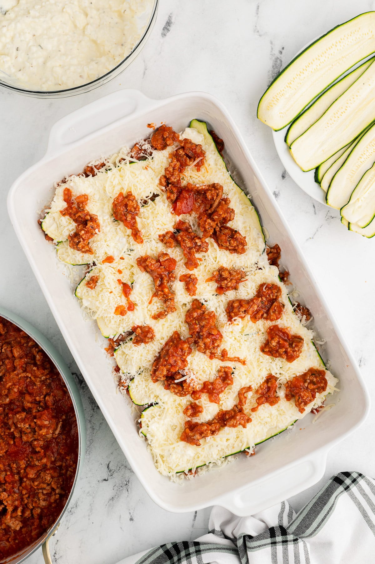 middle layers of sauce for zucchini lasagna being layered in a white casserole dish