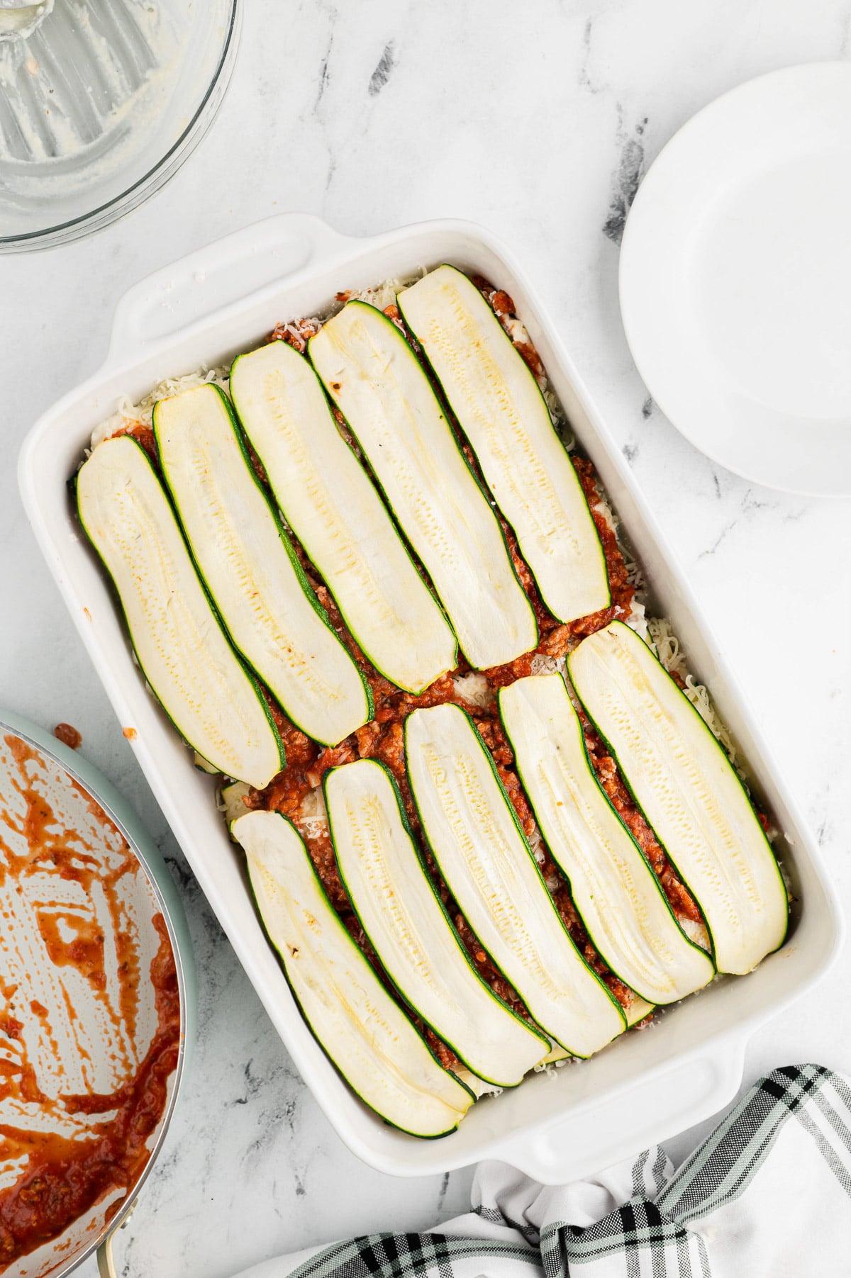 top layer of zucchini slices for zucchini lasagna being layered in a white casserole dish