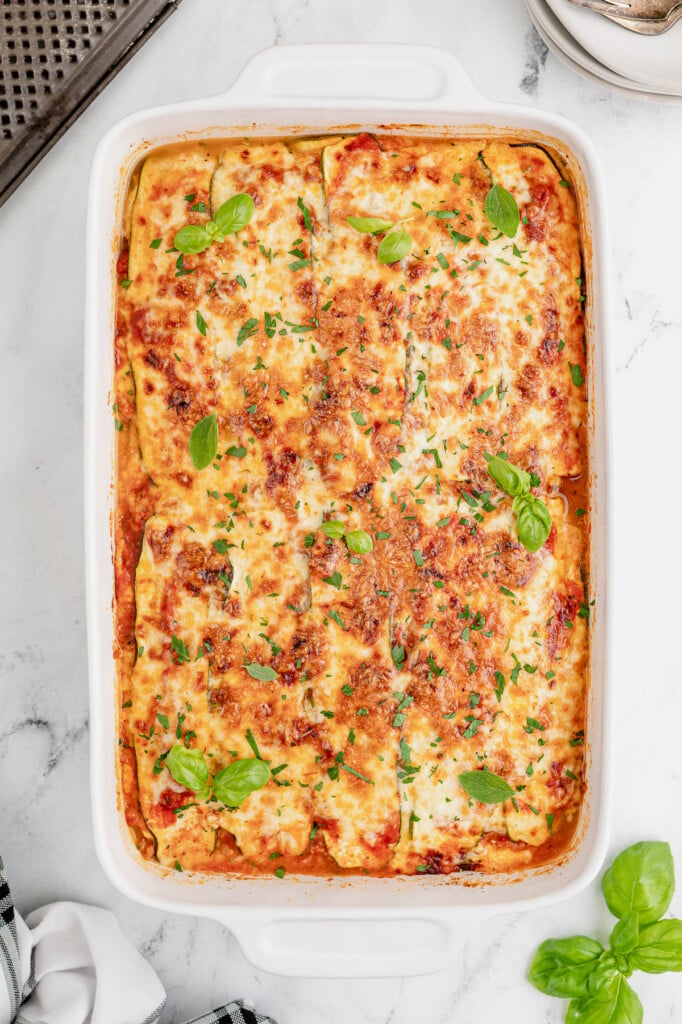 An overhead shot of a white casserole dish of zucchini lasagna on a marble counter
