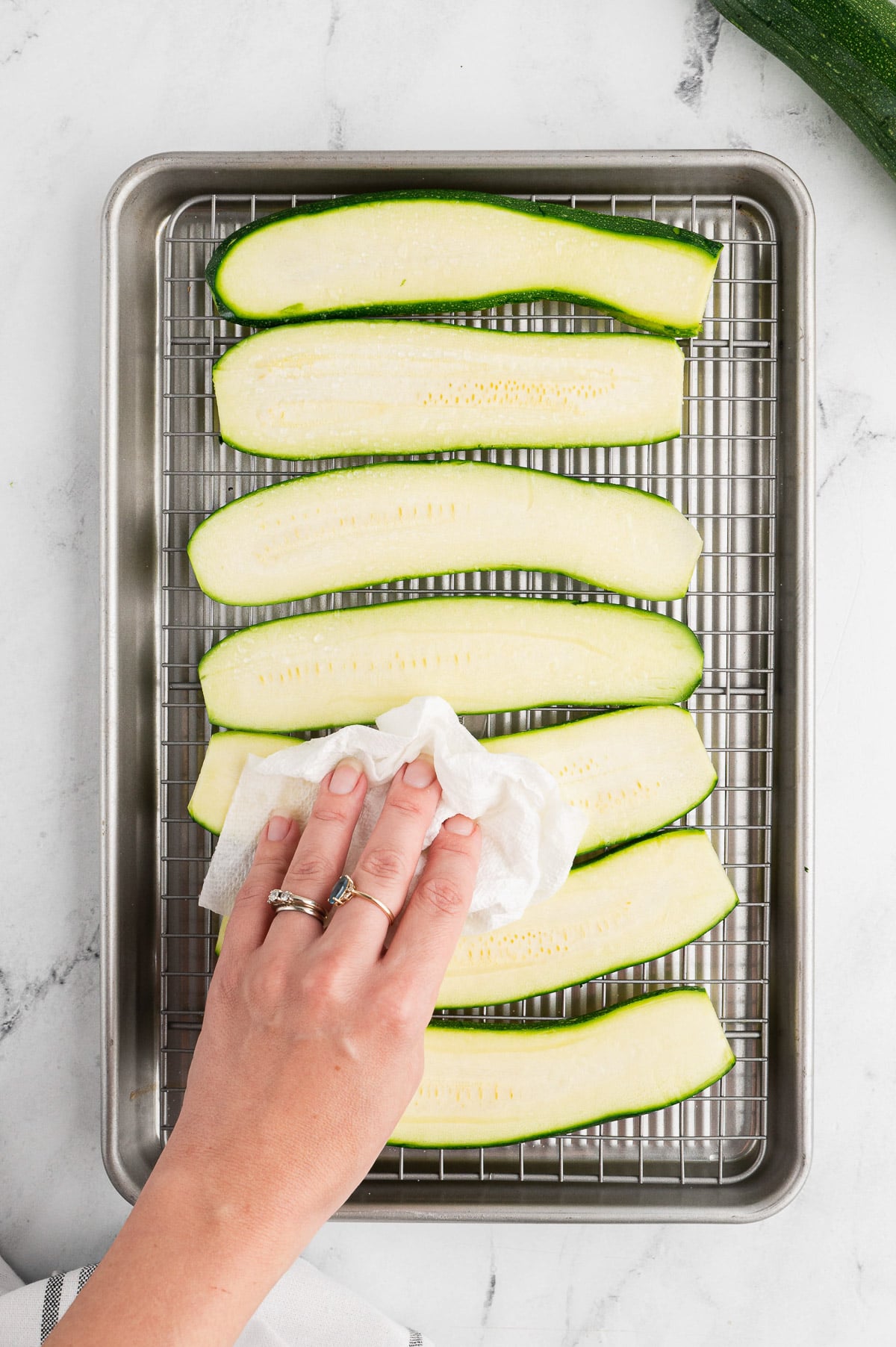 slices of zucchini on a rack on a baking sheet being dabbed with a paper towel to prepare for zucchini lasagna