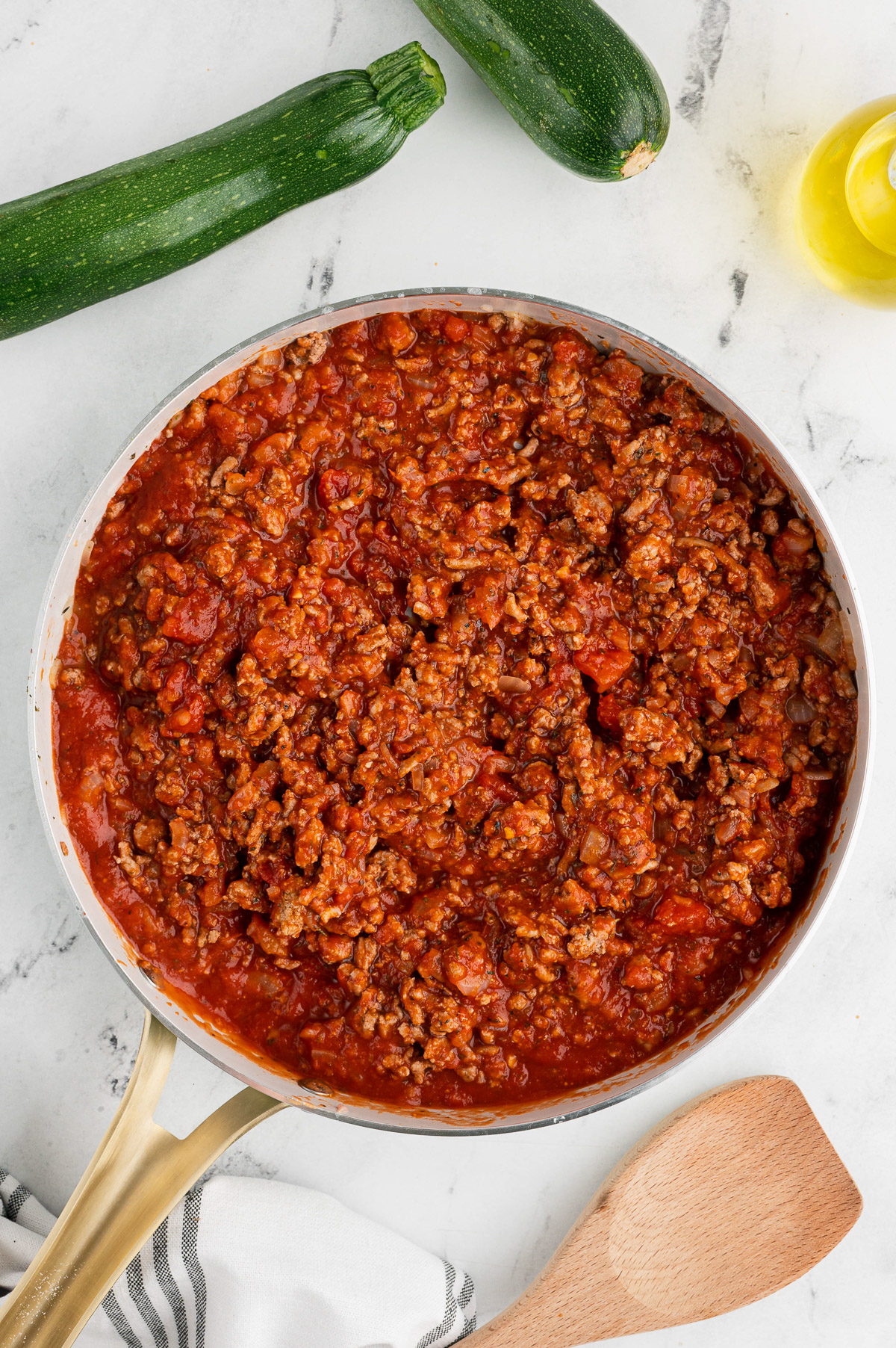 Zucchini lasagna sauce in a pan on a marble counter with zucchini on the side