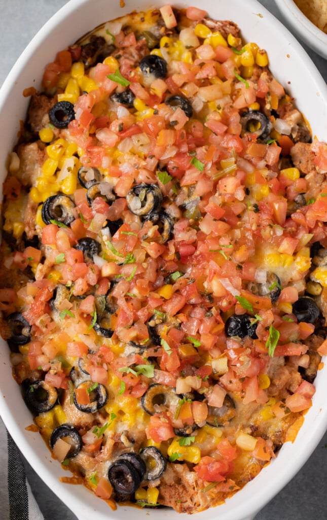 A close up shot of a fully assembled baked seven layer dip in a white baking dish on a grey background