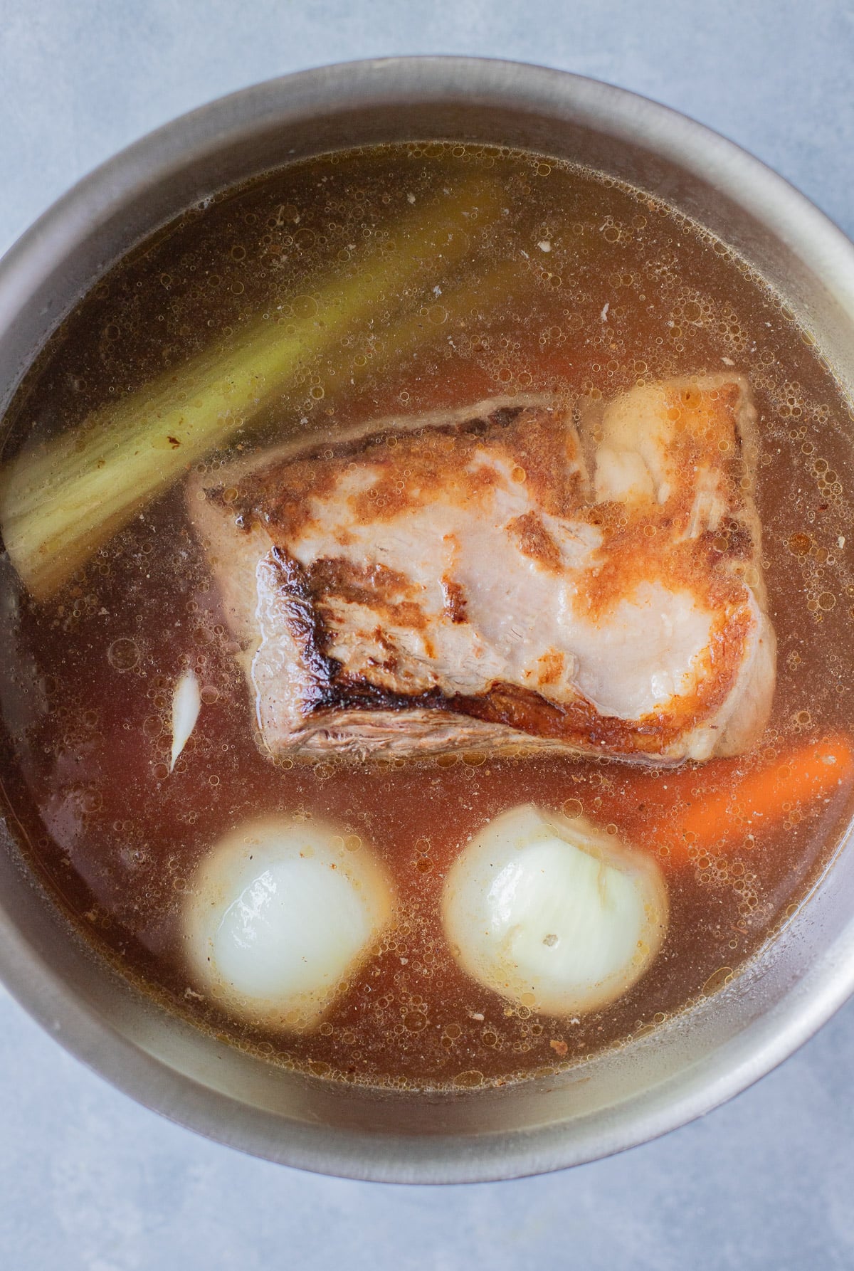 A pot with a beef roast, onions, carrots, celery and broth to make beef soup