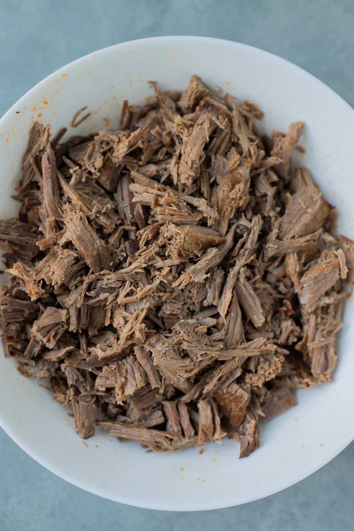 A white bowl of shredded beef for pot roast soup