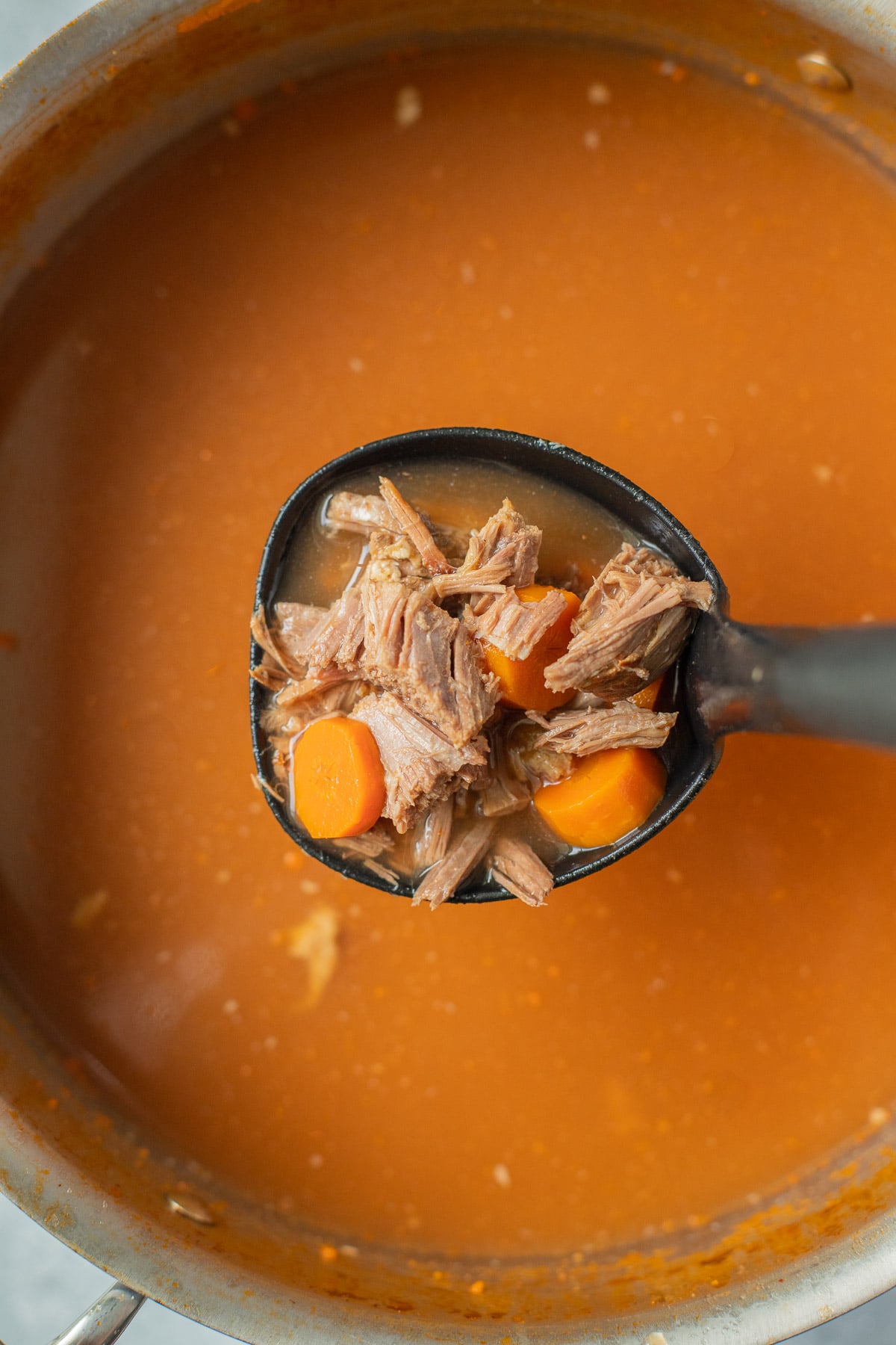 A ladle taking a large scoop of beef soup out of a pot