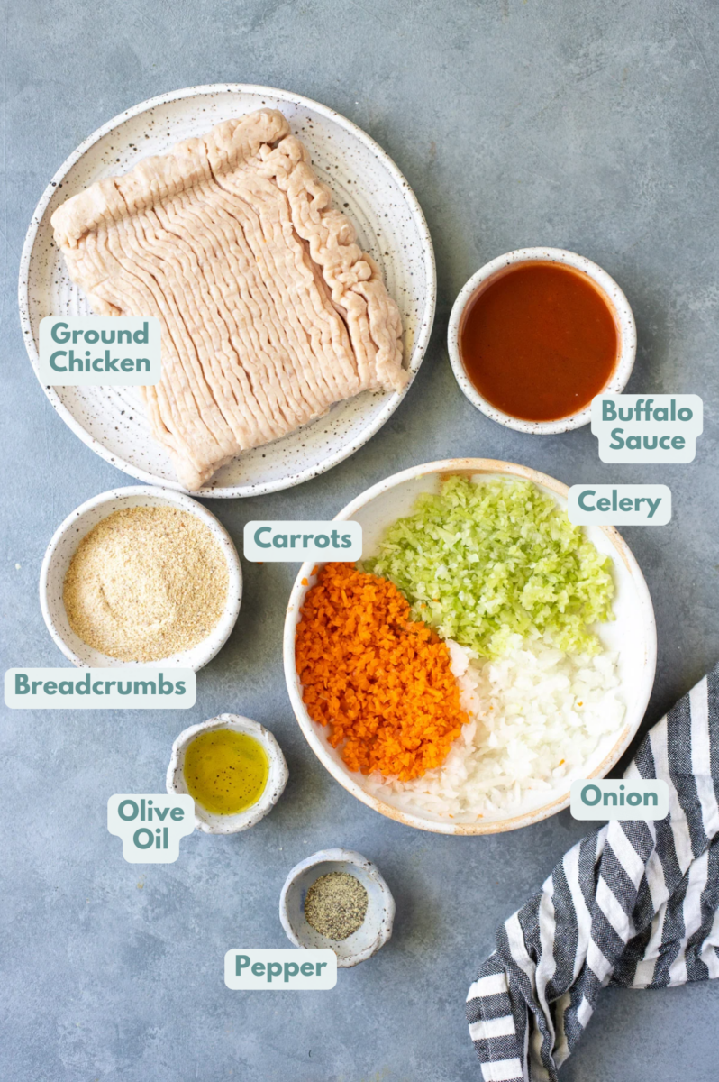 Ingredients for buffalo chicken meatballs in white bowls: ground chicken, carrots, celery, onions, olive oil, buffalo sauce, pepper, bread crumbs, blue cheese 