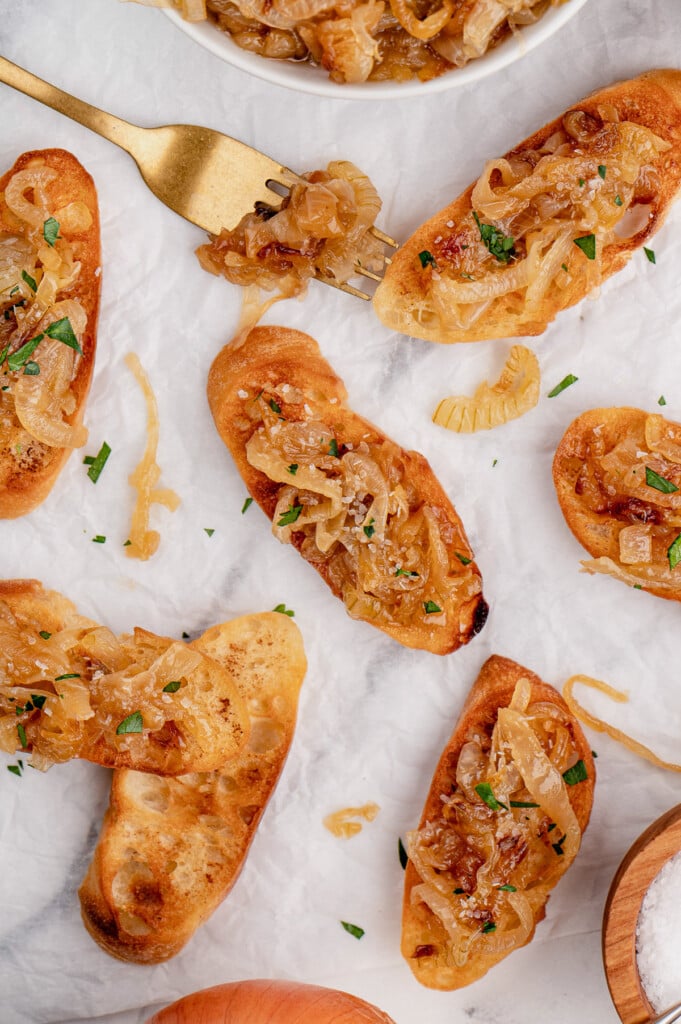 An overhead shot of toasted baguettes topped with caramelized onions on a marble background