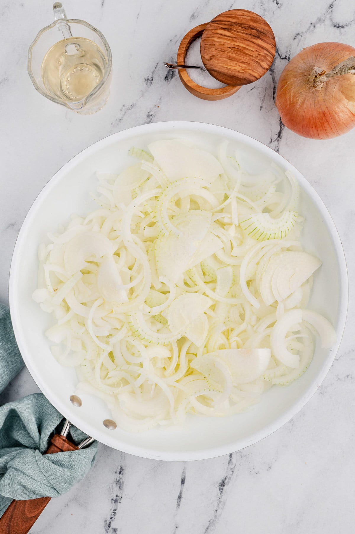A white bowl filled with sliced onions for caramelized onions on a marble background
