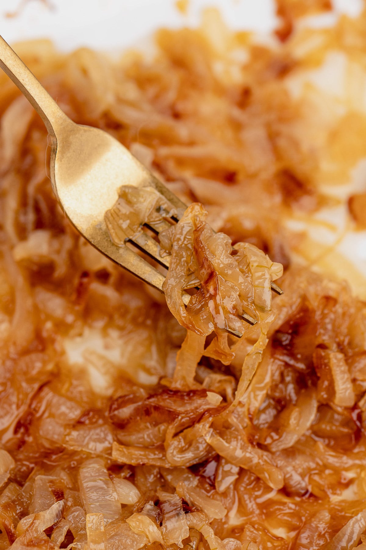 a close up of a fork taking a bite of caramelized onions from a white pan