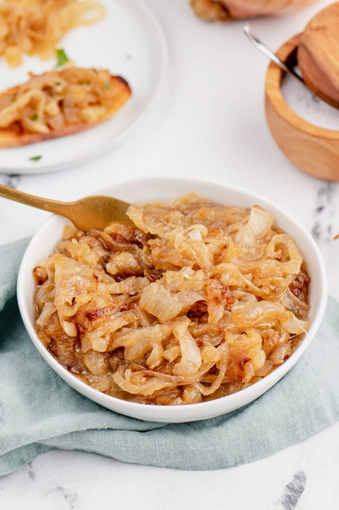A white bowl filled with caramelized onions with a gold fork in it on a marble background with a teal cloth