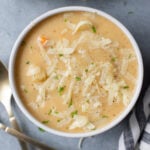 A white bowl of crockpot potato soup with spoons on the side on a grey background