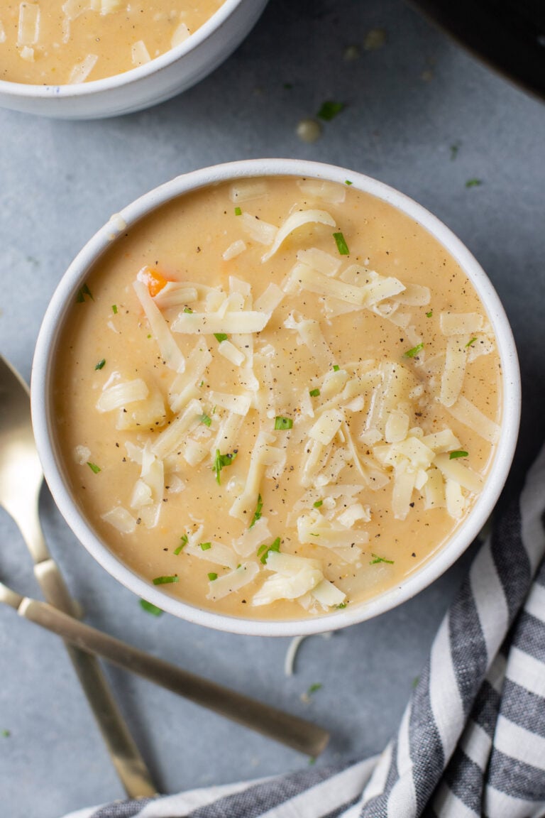 A white bowl of crockpot potato soup with spoons on the side on a grey background