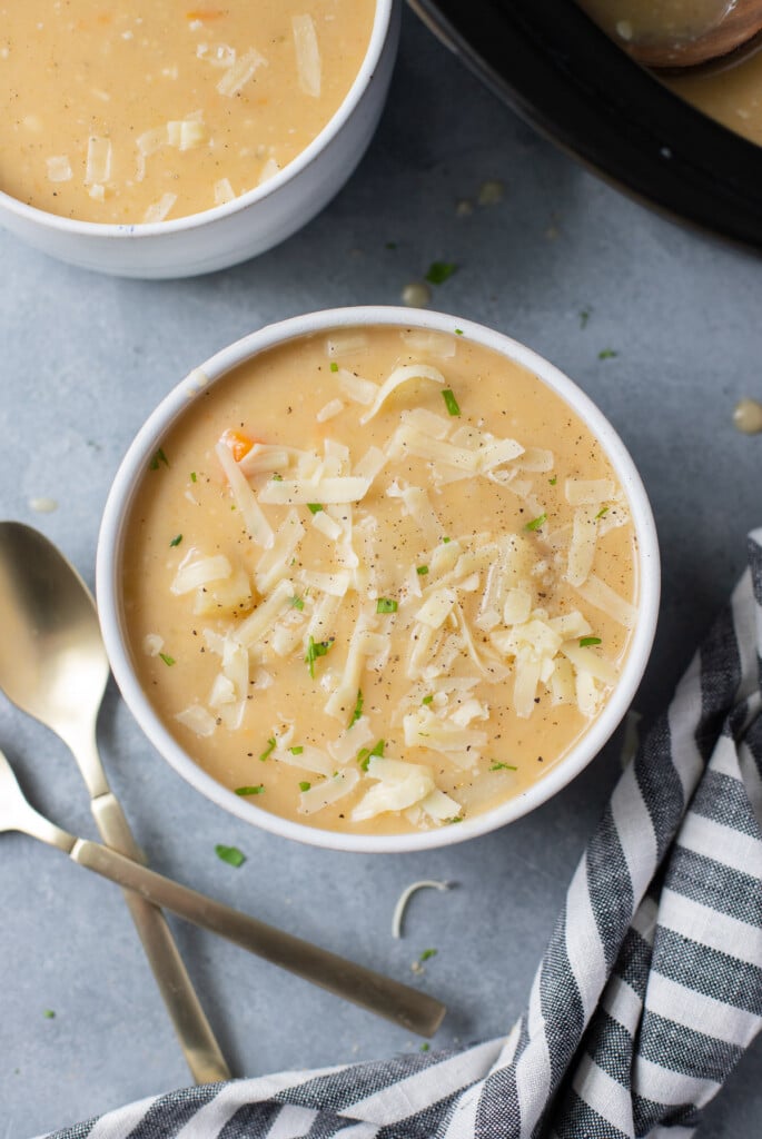 A white bowl of crockpot potato soup with spoons on the side on a grey background