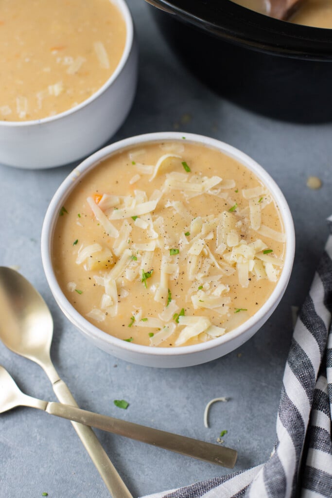 A white bowl of crockpot potato soup with spoons on the side on a grey background