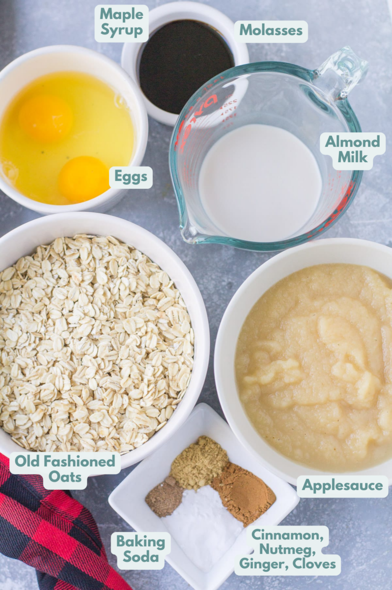 Ingredients for healthy gingerbread muffins on a grey background: old fashioned oats, maple syrup molasses, applesauce, eggs, baking soda, nutmeg, ground ginger, cinnamon, ground cloves, almond milk.