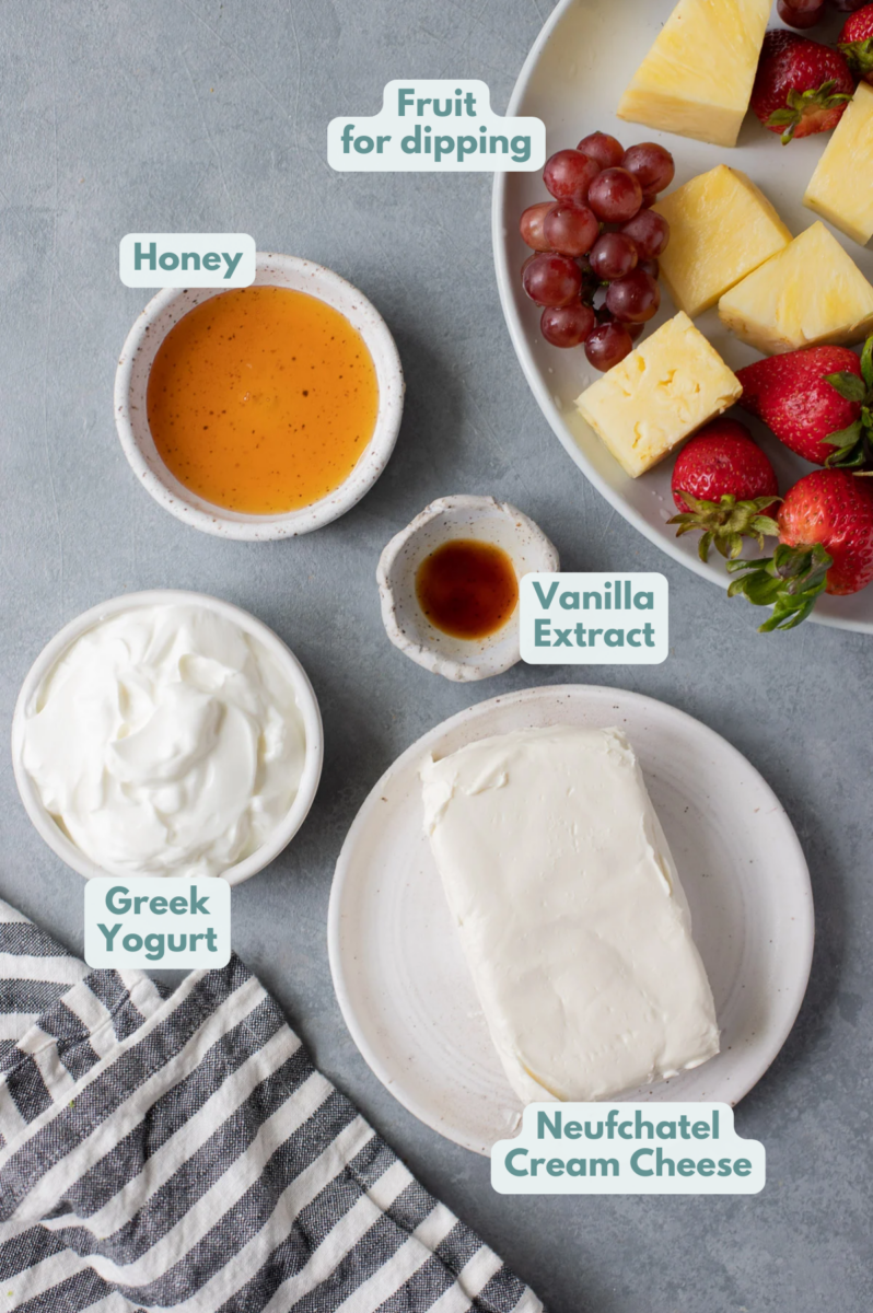 Ingredients for healthy fruit dip in white bowls with a plate of fruit on the side: cream cheese, greek yogurt, vanilla extract, honey