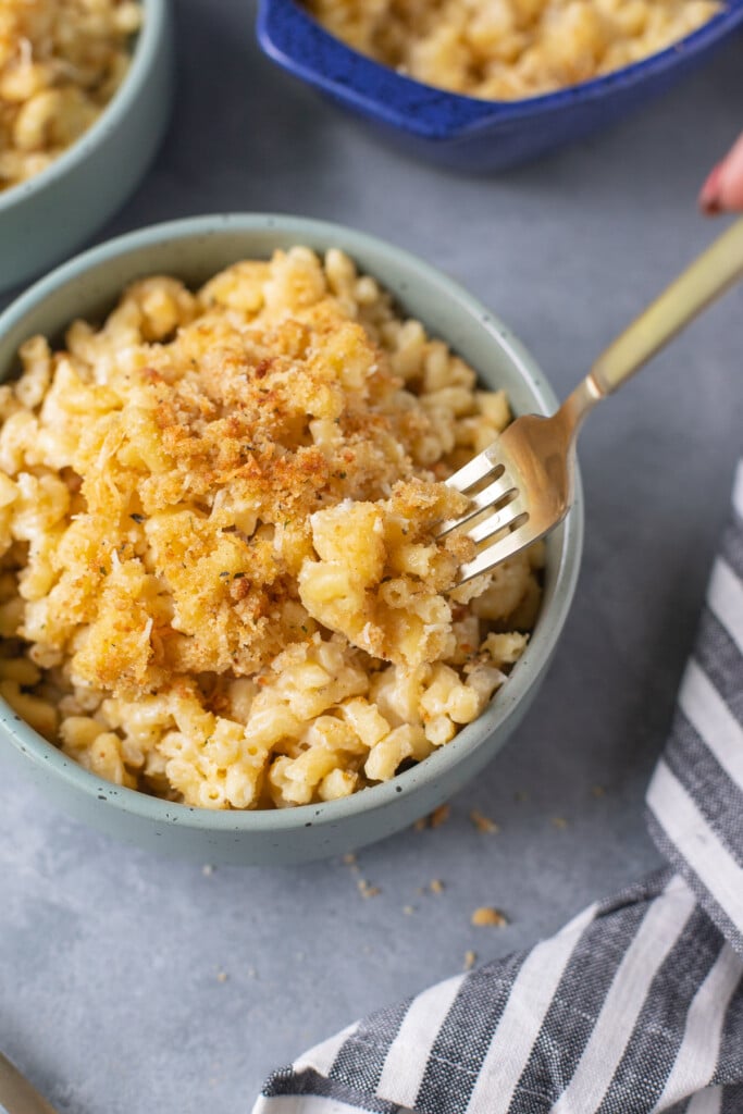 A fork taking a bite of healthy mac and cheese out of a blue bowl on a grey background