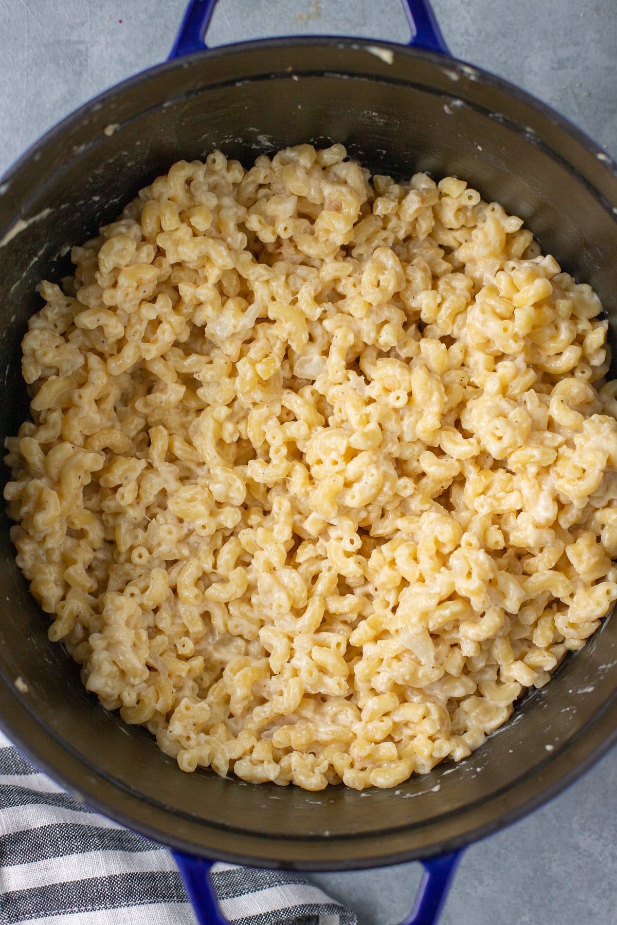 Pasta and cheese sauce tossed together in a black pot on a grey background for healthy mac n cheese