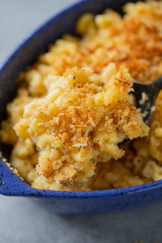 A scoop of healthy mac and cheese being taken out of a blue casserole dish