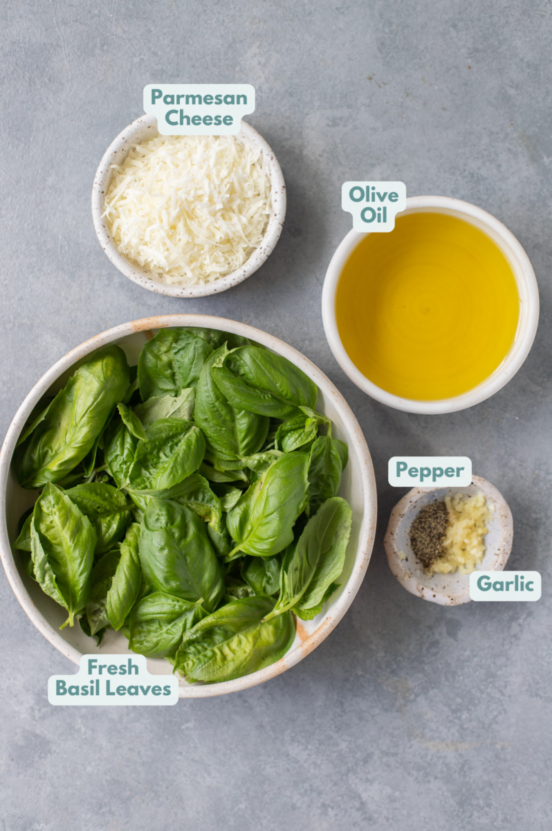 Ingredients for nut free pesto in white bowls: fresh basil leaves, olive oil, parmesan cheese, garlic, pepper