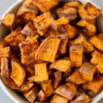 A white bowl of roasted sweet potato cubes on a grey background
