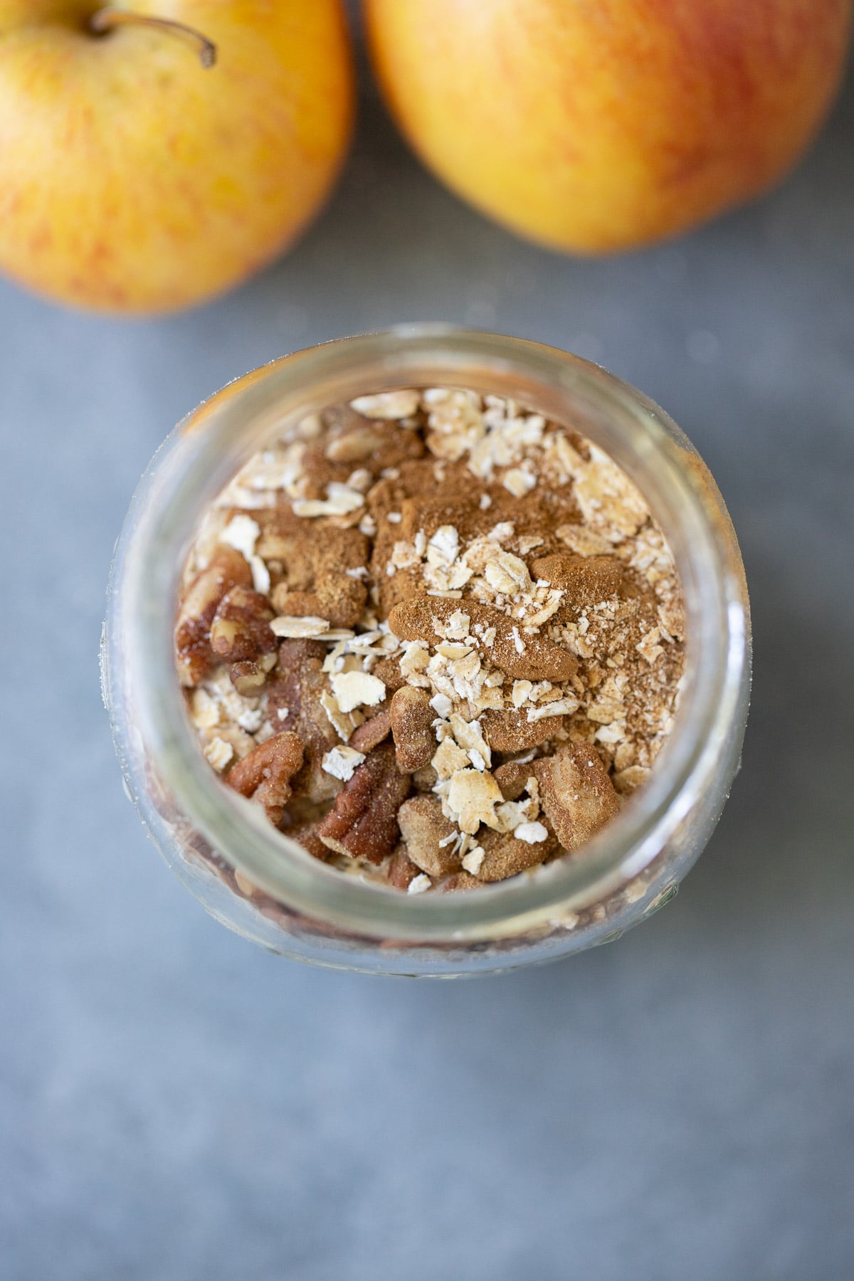 An overhead shot of a mason jar filled with overnight oats before being stirred for apple overnight oats on a grey background