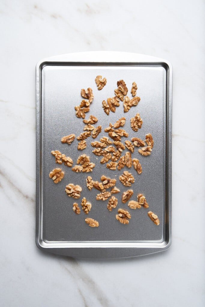 A baking sheet with walnuts on it for roasting for an apple walnut salad