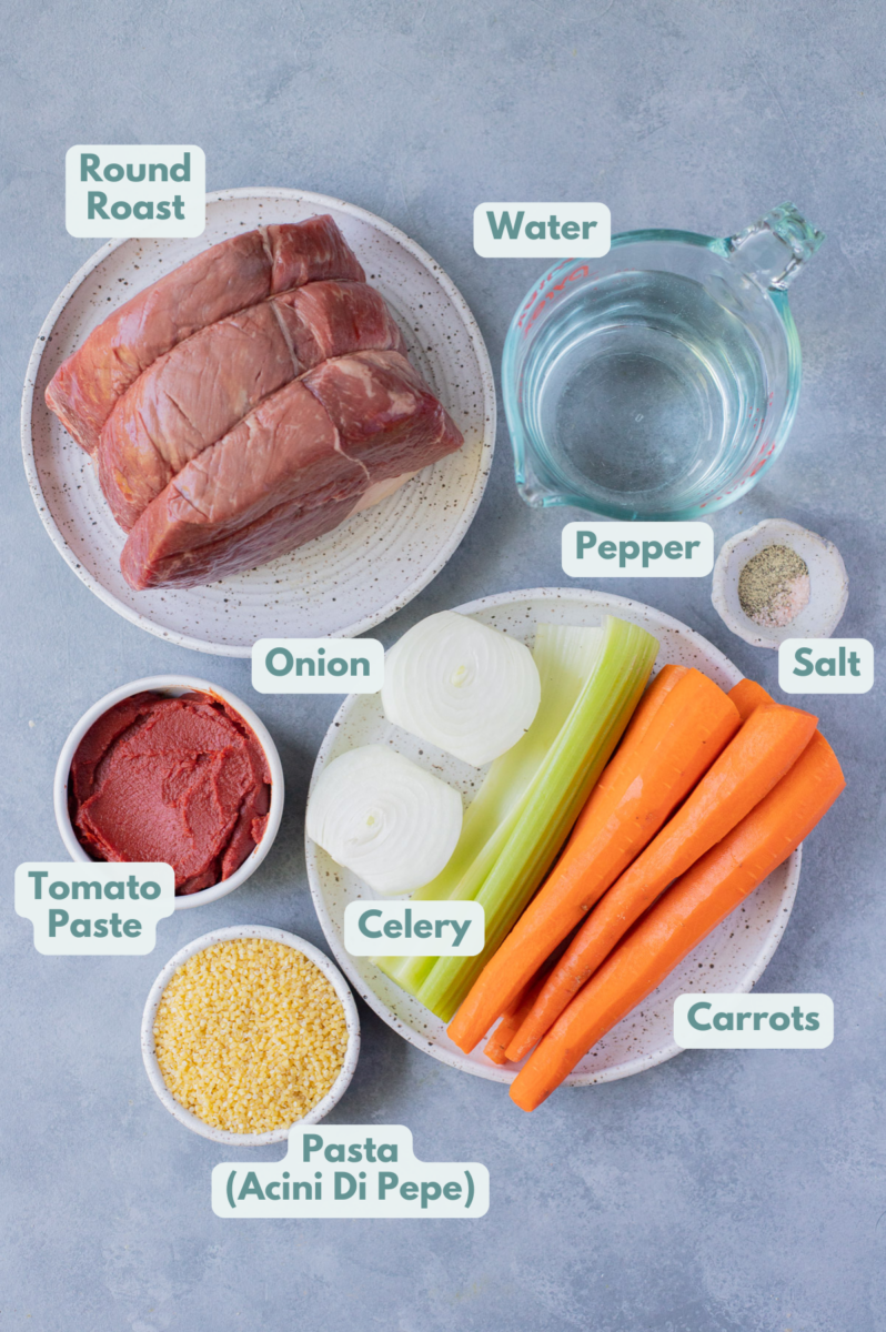 Ingredients for beef soup in white bowls: round roast, olive oil, carrots, celery, onion, tomato paste, pasta, salt & pepper