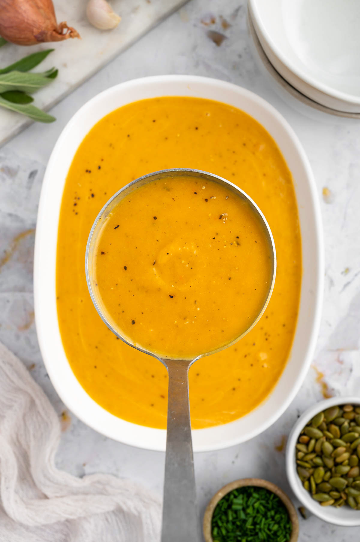 An overhead shot of a white dish of instant pot butternut squash soup with a ladle taking a large scoop out of it on a white background