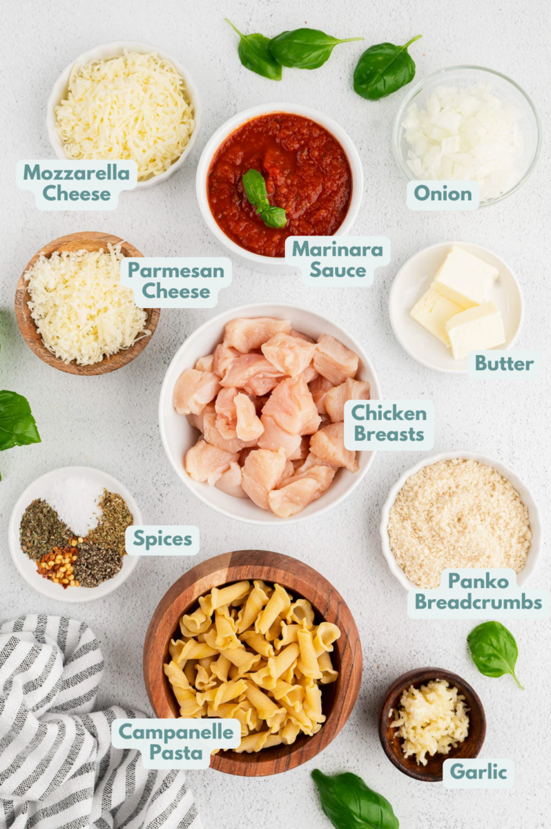 Ingredients for one pot chicken parm pasta in white bowls: butter, garlic, panko, pepper, olive oil, chicken breasts, onion, garlic, dried basil, dried oregano, red pepper flakes, campanelle pasta, marinara sauce, water, mozzarella cheese, parmesan cheese, fresh basil