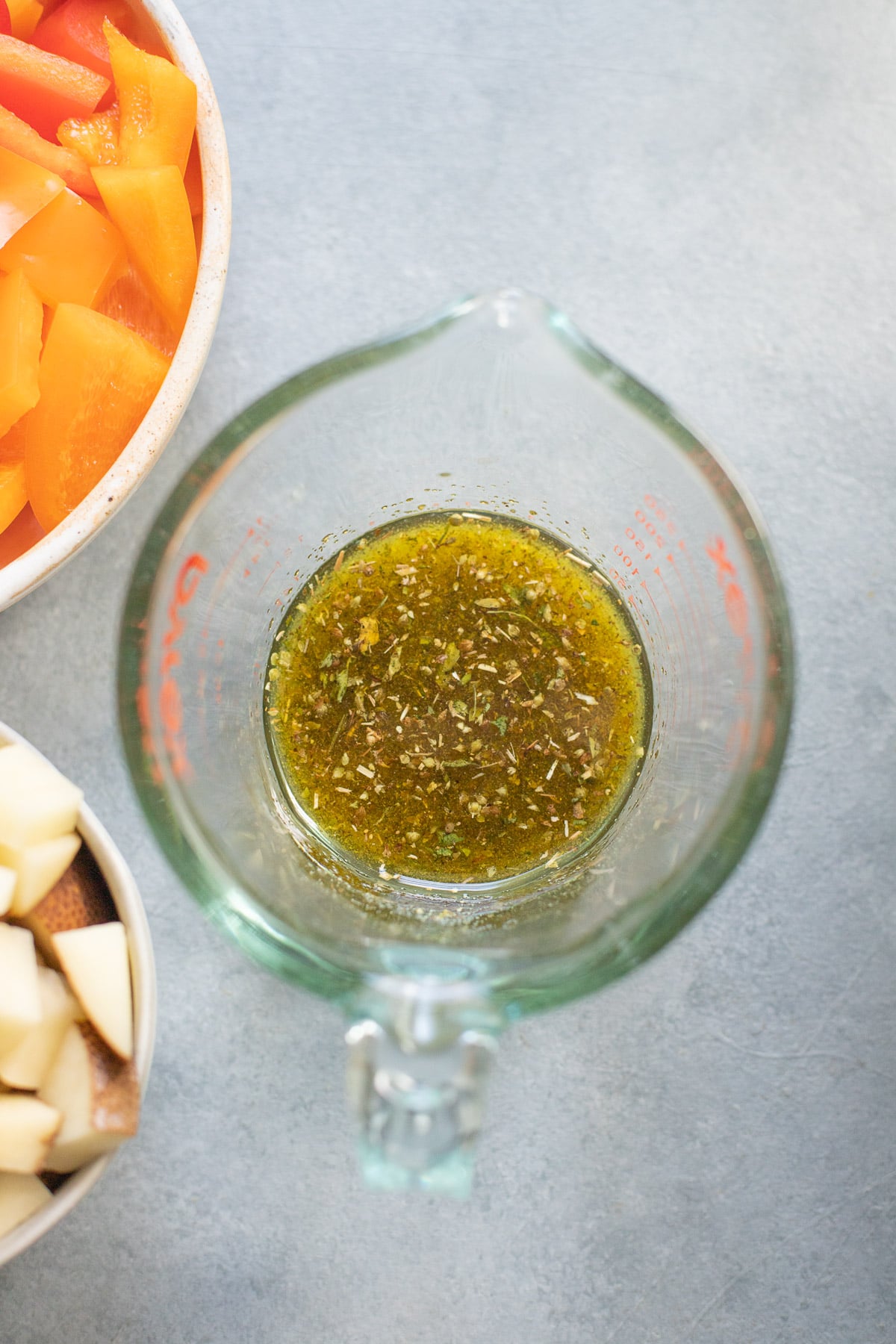 An overhead shot of a clear measuring cup of marinade for greek chicken thighs recipe