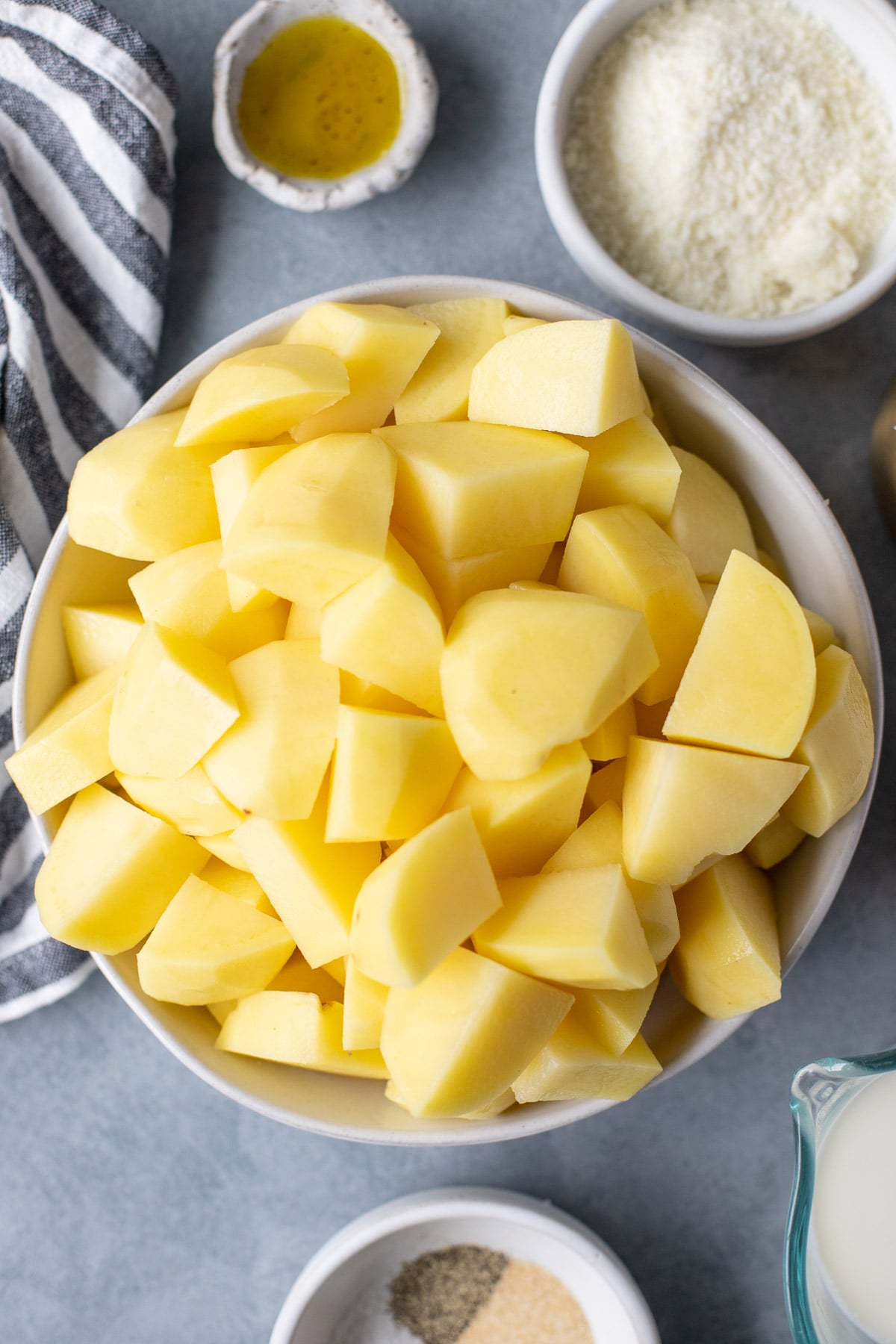 A close up photo of a bowl of peeled and chopped potatoes on a grey background