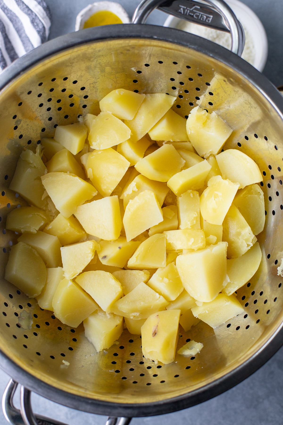A silver colander with boiled, sliced potatoes on a grey background