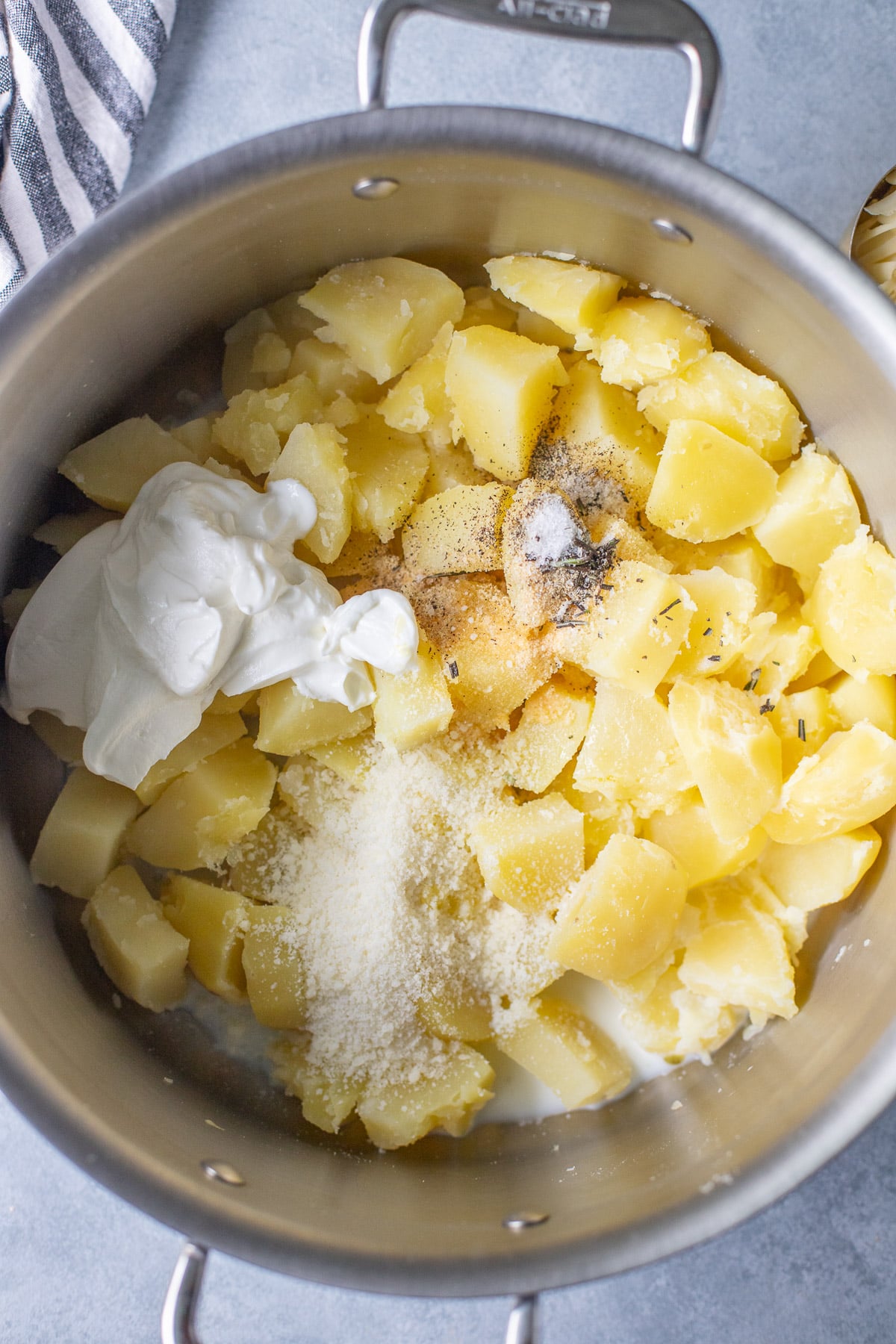 A pot with potatoes and ingredients for mashed potatoes before being mixed on a grey background