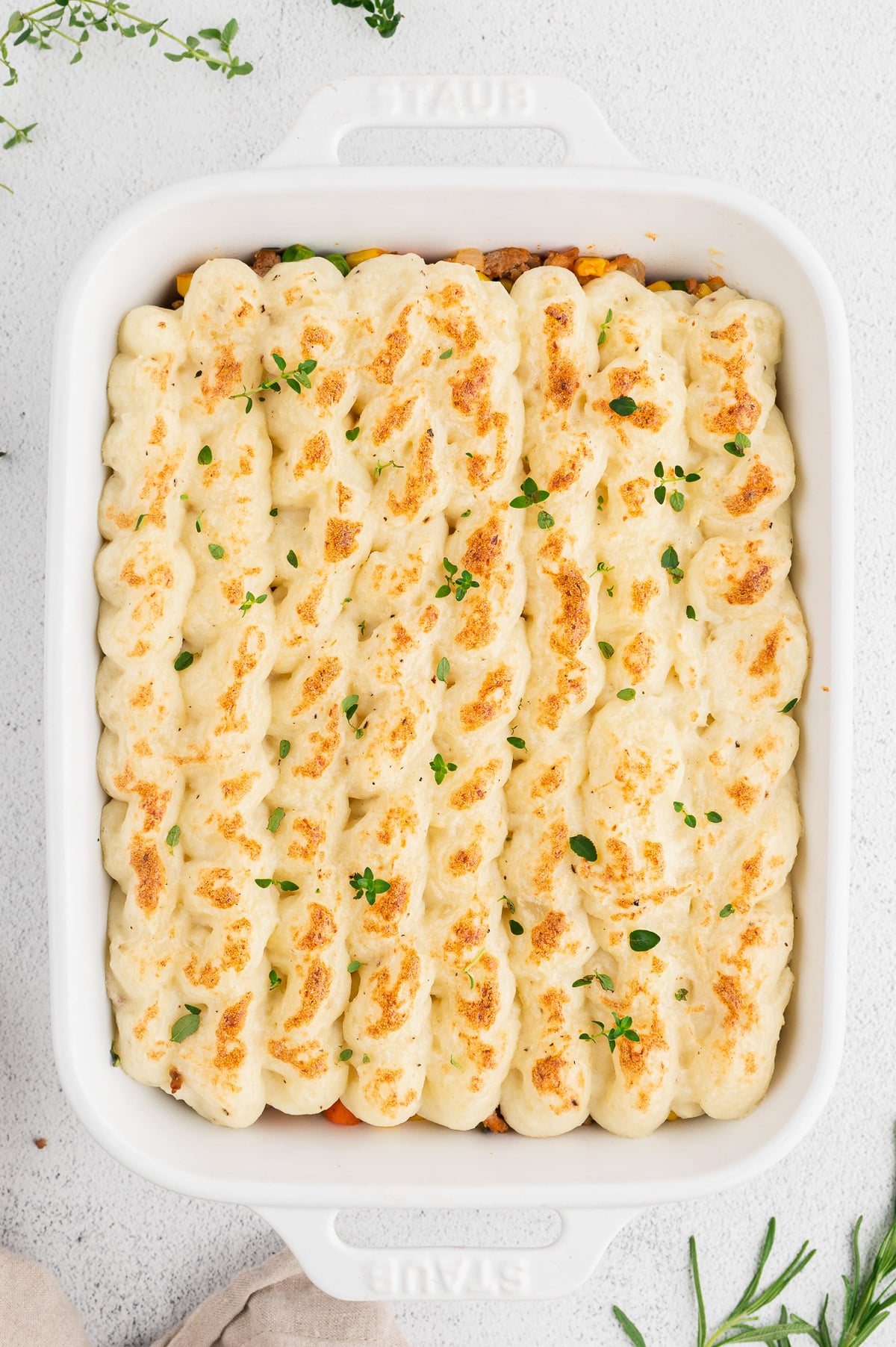 An overhead shot of a perfect healthy shepherd's pie in a white baking dish on a white background