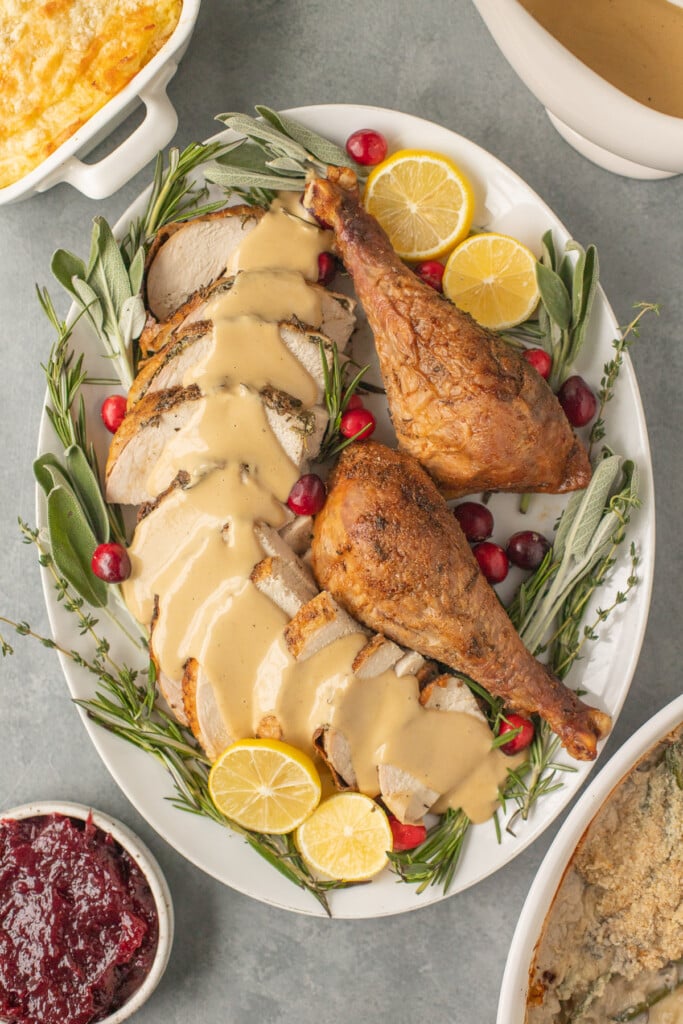 A close up of herb butter turkey on a plate with thanksgiving sides off to the side