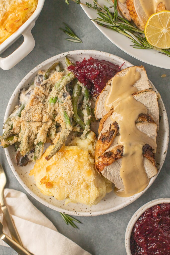 herb butter turkey with mashed potatoes, green beans and cranberry sauce on a white plate