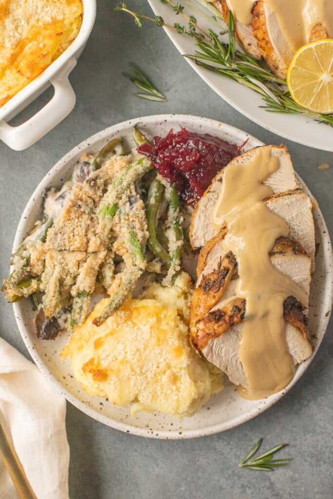 A full thanksgiving dinner on a white plate. turkey, mashed potatoes, green bean casserole and cranberry sauce