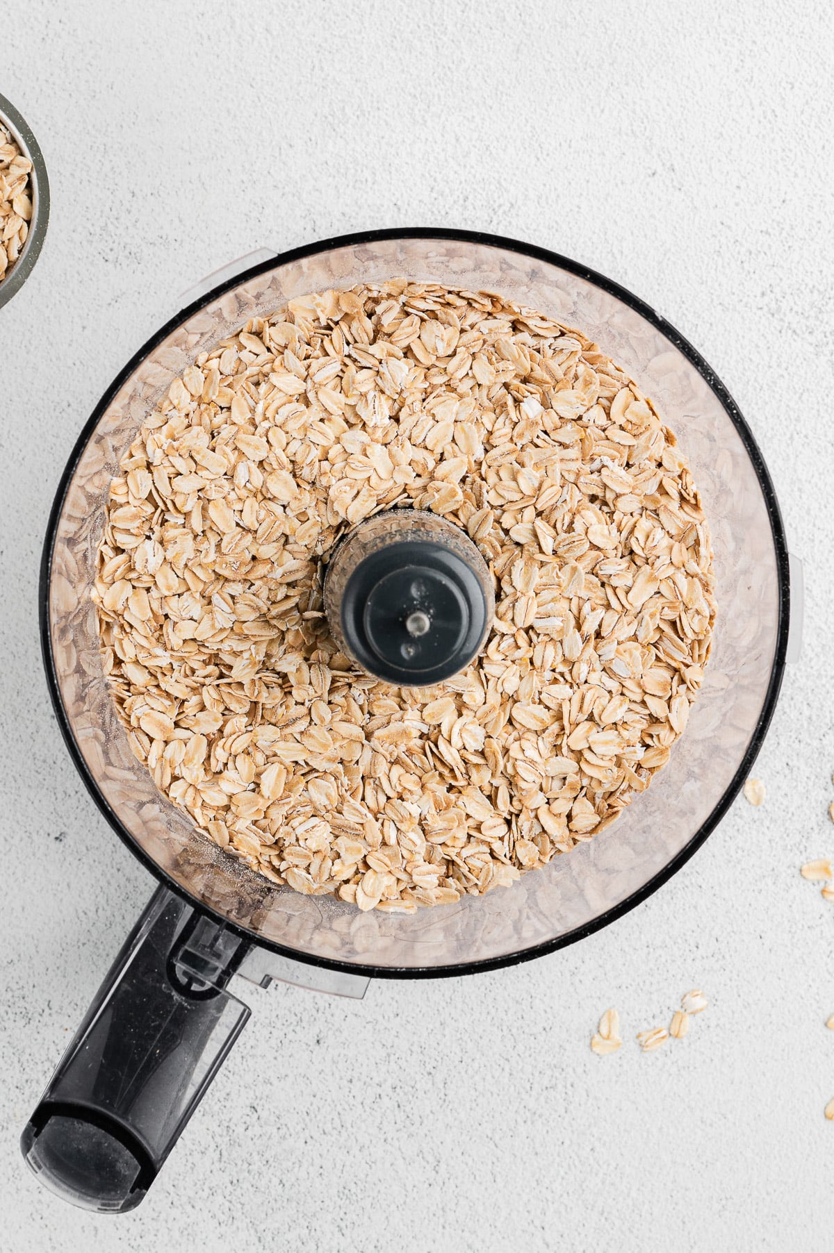 An overhead shot of a food processor with oats in it before pulsing