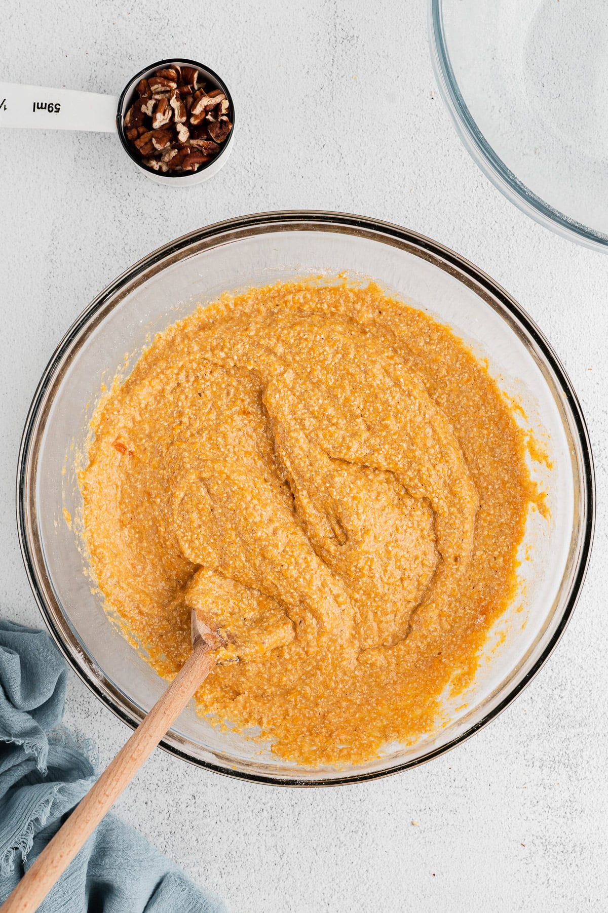 Batter for sweet potato muffins in a clear bowl on a white background with pecans on the side