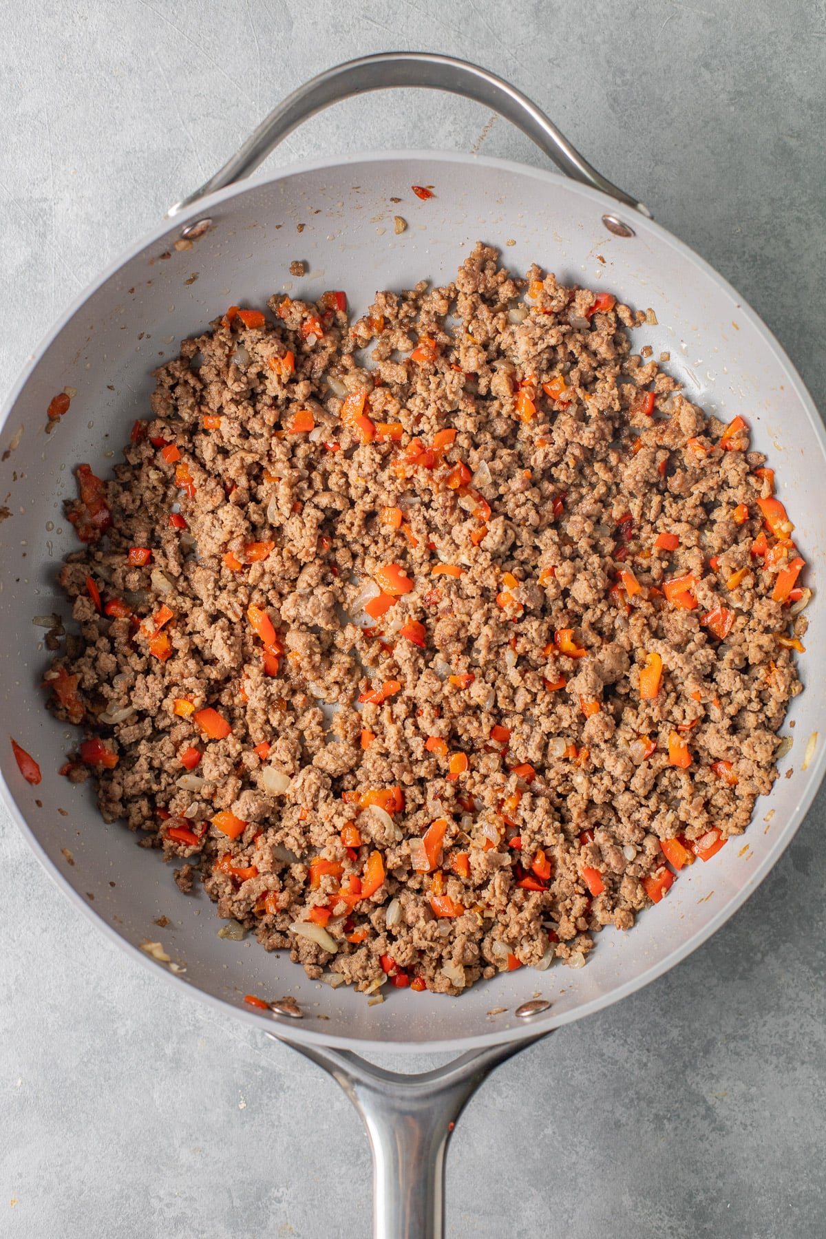 ground beef, peppers and onions browning in a grey pan for taco pasta on a grey background