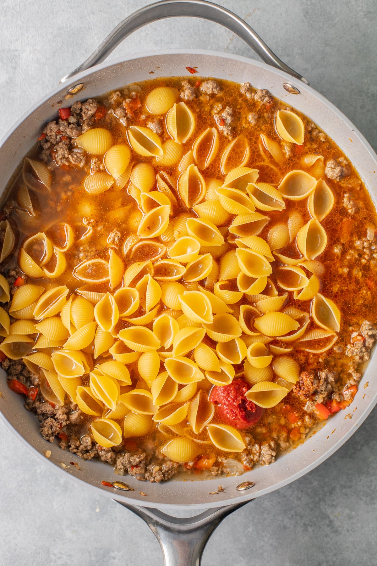 pasta, spices, tomato paste and broth being added to a grey pan for easy taco pasta