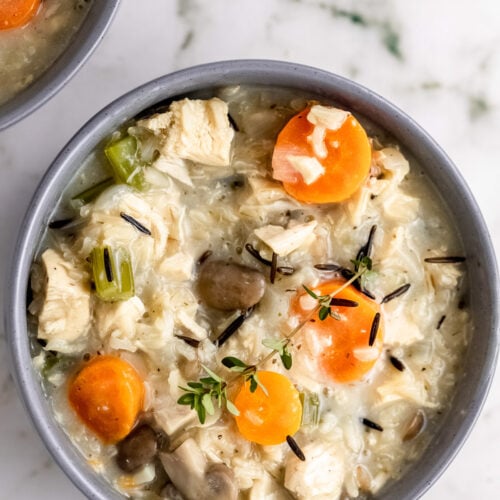 An overhead shot of a grey bowl of turkey wild rice soup with chunks of carrots on a marble background