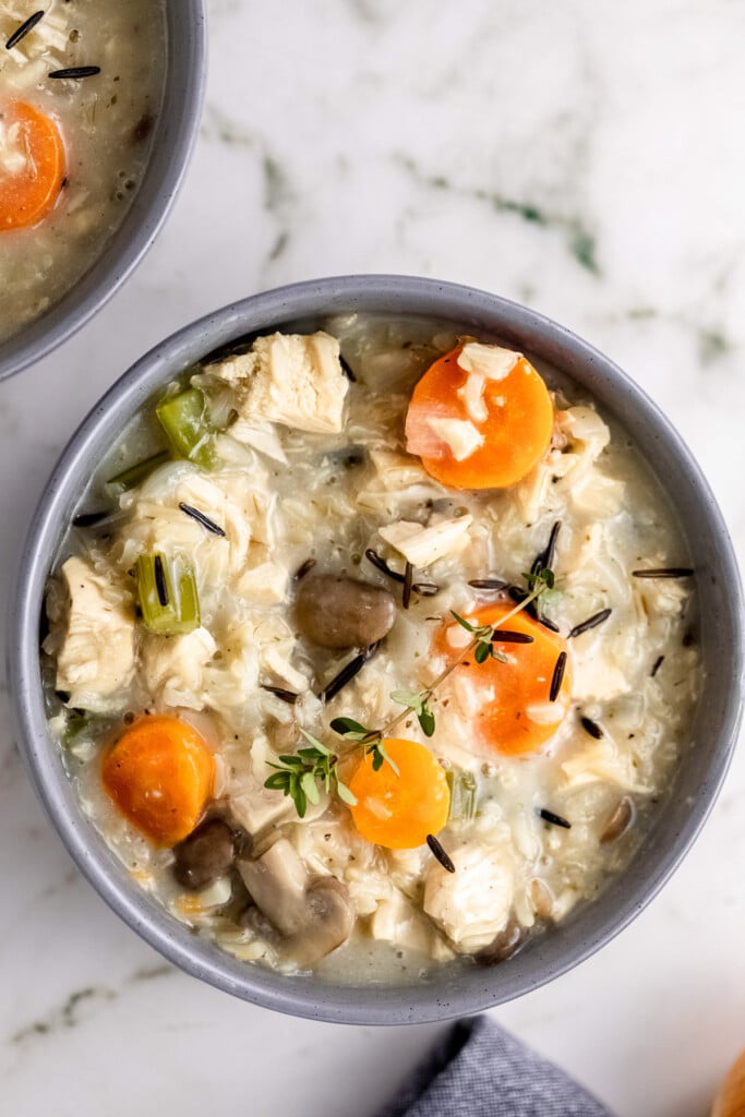 An overhead shot of a grey bowl of turkey wild rice soup with chunks of carrots on a marble background