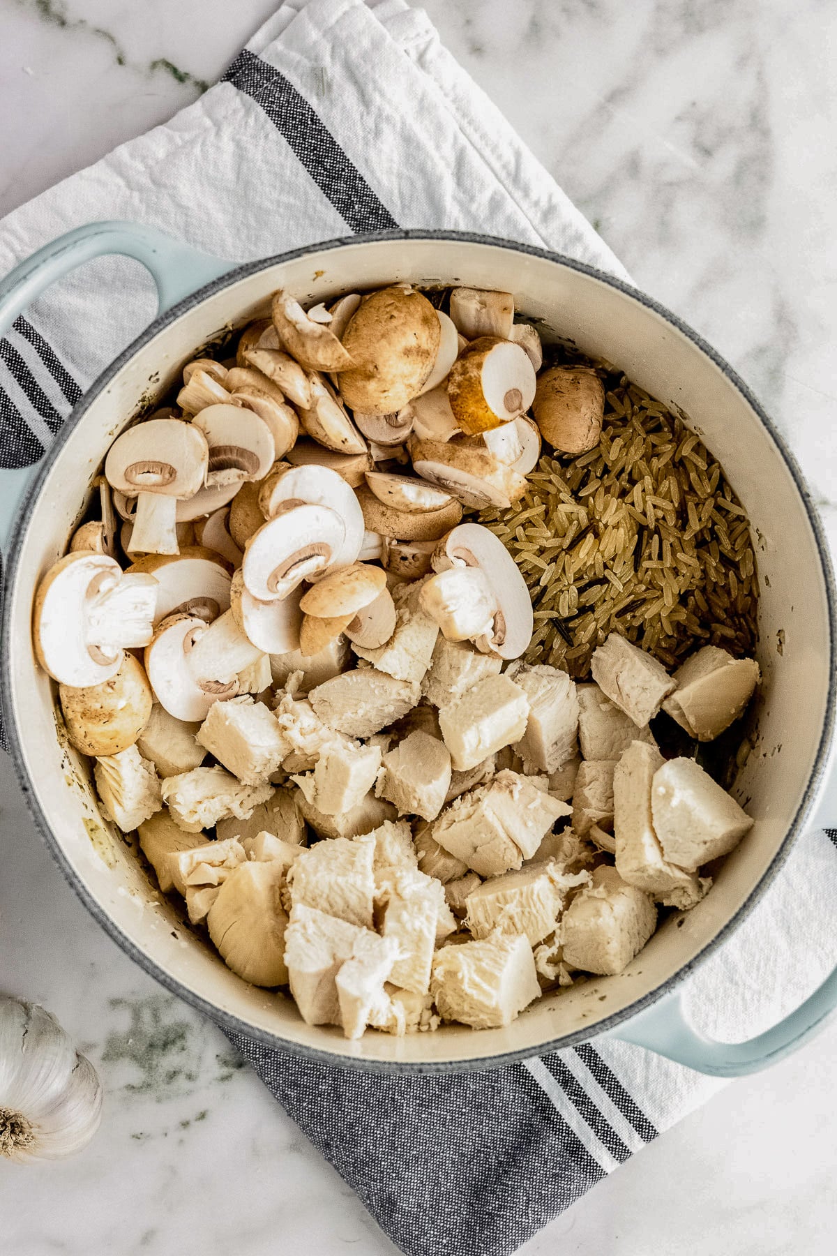 A large pot with turkey, mushrooms, and wild rice on top of veggies for turkey wild rice soup