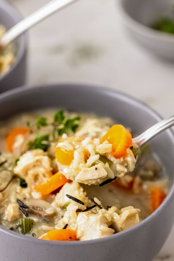 A spoon taking a bite out of a grey bowl of turkey wild rice soup